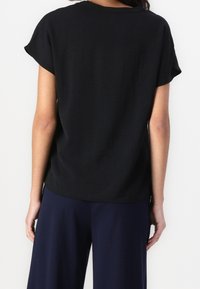 Haut noir à manches courtes avec une coupe décontractée, doté d'un col arrondi et d'une texture douce, associé à un pantalon bleu marine à jambes larges.