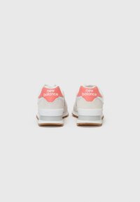 Baskets blanches et roses avec une tige en cuir suédé et mesh, présentant un logo visible sur le talon et une semelle extérieure en caoutchouc pour une bonne adhérence.