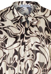 Jedwabna bluzka w kolorze kremowym z brązowym abstrakcyjnym wzorem. Posiada kołnierzyk z kokardą oraz pionowe paski z delikatnymi metalicznymi akcentami.