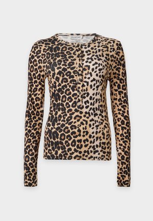 Mulher vestindo uma blusa de manga comprida com estampa de leopardo combinada com calças pretas de perna larga e sapatos pretos pontiagudos, em pé com uma mão no bolso.