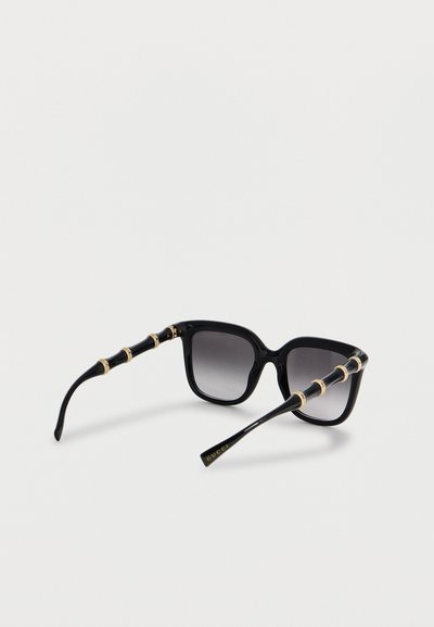 Μαύρα τετράγωνα γυαλιά ηλίου με βαθμιδωτούς φακούς και υφασμένα μπράτσα με χρυσές λεπτομέρειες σε μορφή δαχτυλιδιών και το λογότυπο «Gucci» σε ένα από τα μπράτσα.