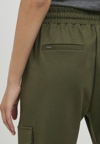 Groene katoenen joggers met een elastische tailleband, zijzak en een klein metalen logoaccent op de achterzak. Gladde textuur.