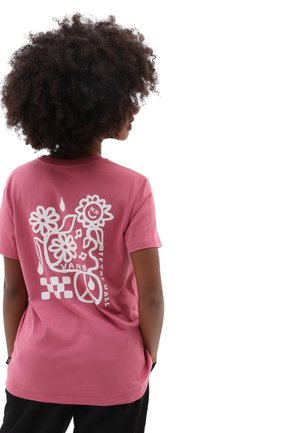 Person mit lockigem Haar trägt ein pinkes T-Shirt mit weißen grafischen Blumen, Peace-Zeichen, Musiknoten und Text auf dem Rücken.
