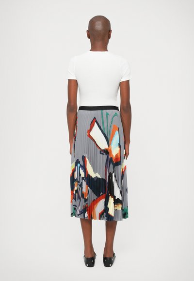 Top alb, ajustat, cu maneci scurte, asortat cu o fustă plisată care prezintă un model abstract colorat pe un fundal gri.