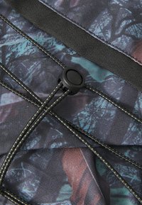 Close-up van een gestructureerde stof met een multikleurig geometrisch patroon, met een zwarte verstelbare koordsluiting en versterkte stiksels voor duurzaamheid.