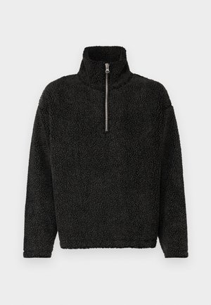 Pull noir en polaire avec un col haut et une fermeture éclair au quart à l'avant. Dispose d'un tissu doux et texturé ainsi que de manches longues.