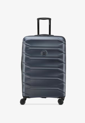 Valise rigide gris foncé avec quatre roues et une poignée télescopique noire déployée.