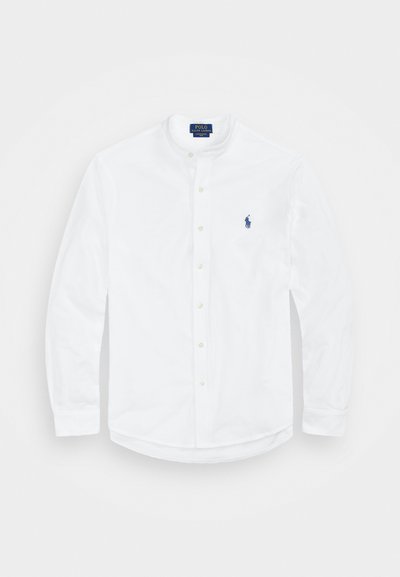 Balta ilga rankovė marškiniai su stovelio apykakle, sagų priekis ir mėlynas logotipas kairėje pusėje. Pagaminti iš lygios medvilnės audinio.