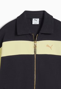 Čierna bunda so širokým horizontálnym svetložltým pruhom, zlatým zipsom a vyšitým zlatým logom Puma na hrudi.