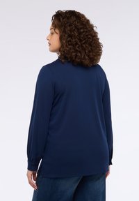 Camicia a maniche lunghe blu navy in tessuto liscio con una vestibilità rilassata, caratterizzata da polsini con bottoni e spacchi laterali sull'orlo per una maggiore libertà di movimento.