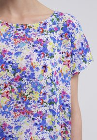 Bloemend T-shirt van lichtgewicht stof, met een mix van blauwe, roze en gele bloemen, met een ronde halslijn en korte mouwen.