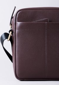 Brown leather bag with a textured finish, featuring a front pocket and a black adjustable strap. Includes gold-tone hardware accents.