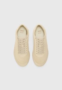 Beige suede sneakers with a rounded toe, flat laces, and a slightly textured sole. Brand logo visible on the tongue.