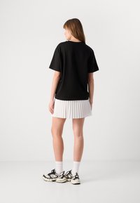 Svart t-skjorte med korte ermer og avslappet passform, kombinert med et hvitt plisségjort. Outfitten fullføres med klumpete svarte og hvite sneakers.