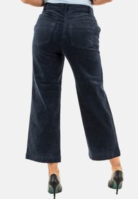 Pantaloni a zampa d'elefante in corduroy blu scuro con tasche posteriori e superficie testurizzata, abbinati a tacchi alti neri.