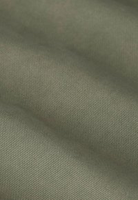 Close-up van een gladde olijfgroene stof met fijne verticale ribbeltextuur en subtiele plooien.