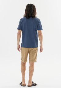 Blå kortärmad t-shirt med rund halsringning, tillsammans med ljusbruna uppvikta shorts och mörka slip-on sandaler. Slät tygkvalitet, avslappnad passform.
