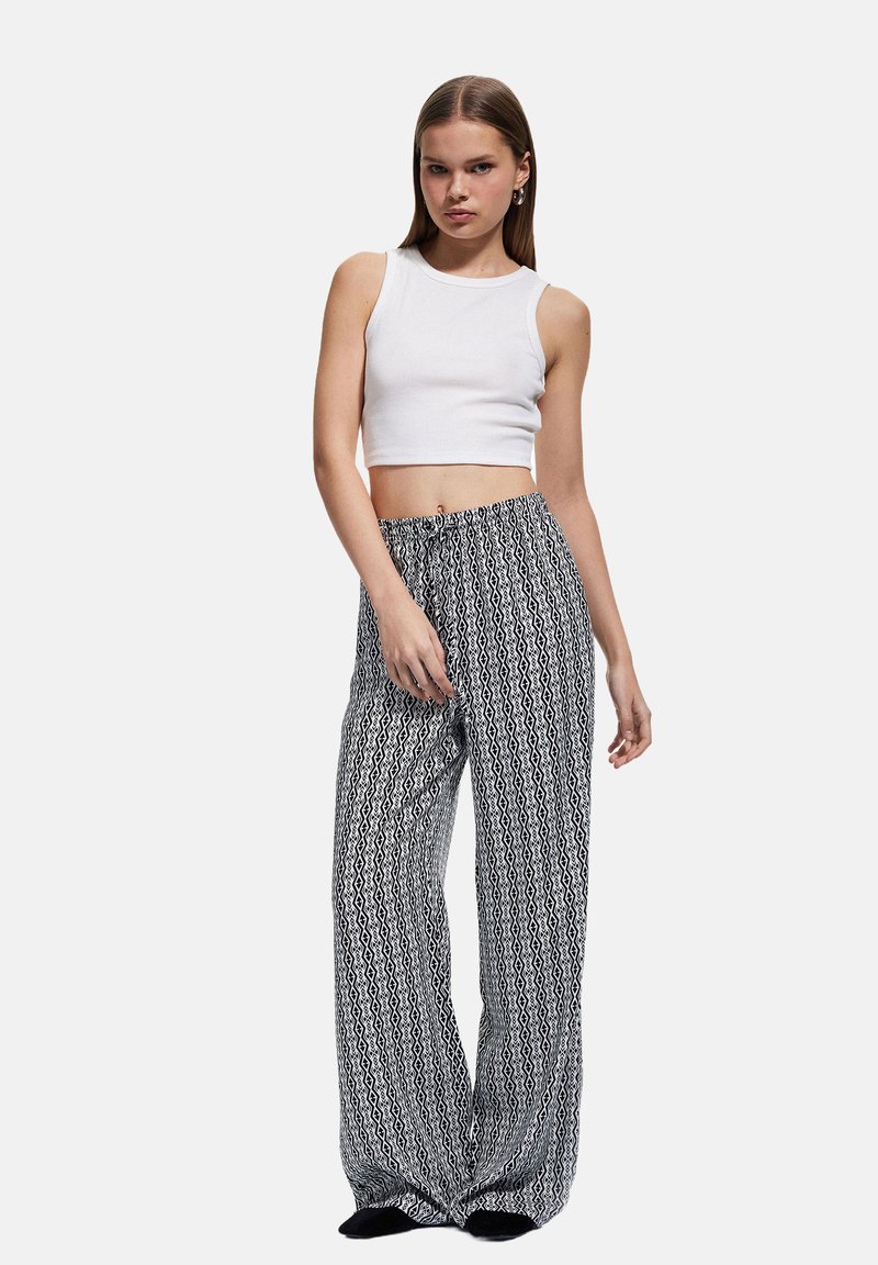 Weißes geripptes Crop-Top kombiniert mit legeren, weit geschnittenen Hosen in schwarz-weißem Muster. Mit elastischem Bund und fließendem Stoff.