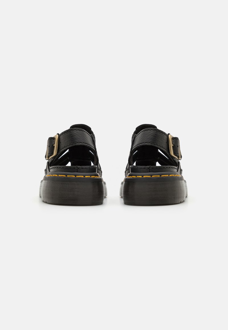 Black leather sandals with crisscross design, buckle strap, and textured black sole; yellow stitching along the sole's edge.