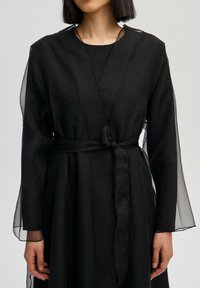 Must kleit, millel on pikad läbipaistvad varrukad ja seotud vöökand. Kangas on tekstuurse välimusega. Lihtne kaelus ja minimalistlik disain.