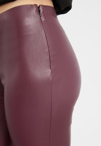 Burgundské kožené legíny s vysokým pasem s elegantním designem, obsahující skrytý zip vzadu a hladký, strukturovaný povrch.
