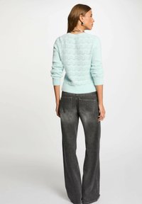 Maglione azzurro chiaro lavorato a maglia con un motivo a onde, abbinato a jeans grigi a gamba larga. Il maglione ha maniche lunghe e polsini a costine, design casual.