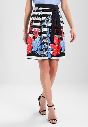 Black and white striped skirt with large red and blue floral prints, paired with black ankle-strap high heels.