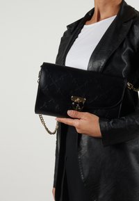 Black leather crossbody handbag with quilted pattern, gold hardware, and chain strap. Front flap closure with heart-shaped accent.