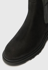 Bottine noire en cuir lisse avec un bout arrondi, des panneaux latéraux texturés contrastants et une semelle en caoutchouc robuste.