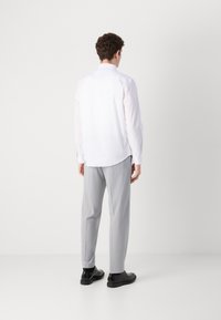 Weißes Langarmhemd mit Rücken-Schlitz, kombiniert mit hellgrauen Hosen und schwarzen Schuhen. Glatte Textur und klassisches Kragen-Design.