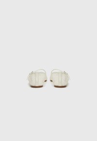 Ballerines en filet blanc avec une semelle plate, des sangles arrière et un embout arrondi. Présentent un design texturé et des accents matériels minimaux.