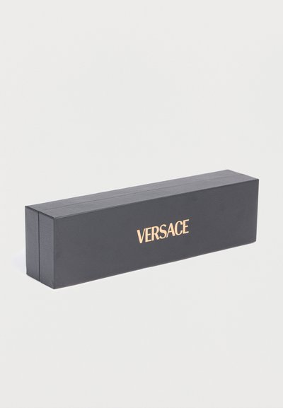 Longue boîte rectangulaire noire Versace avec texte doré centré sur le côté, placée sur un fond blanc.