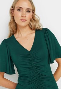 Blusa verde con escote en V y mangas cortas abullonadas; presenta un detalle de frunce en el centro, hecha de una tela suave y elástica.