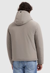 Lichtbeige gewatteerde jas met een capuchon, met een gestroomlijnd ontwerp, textuurstof en een kleine driehoekige accent op de rug.