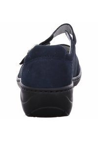 Marineblauwe suède schoen met een zwarte rubberen zool, met een slingback ontwerp en een zachte textuur. Geaccentueerd door een eenvoudige, verstelbare band bovenop.