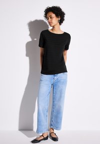 Haut noir texturé à manches courtes assorti à un jean à jambes larges bleu clair et des ballerines noires. La tenue est décontractée et présente un décolleté en scoop.