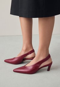 Bordó bőrből készült slingback magassarkú cipő hegyes orral, alacsony blokksarkú, és oldalain kivágásokkal a minimalista megjelenésért.