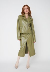 Veste en cuir synthétique vert olive, courte, avec fermeture éclair et poche avant, associée à une jupe assortie de longueur genou dotée d'une fente.