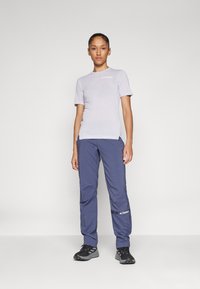 T-shirt corta de cor roxa clara com o logótipo "TERREX", combinado com calças azul-escuras com um bolso e detalhes refletivos. Botas de caminhada pretas.