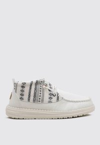 Zapatos blancos con una parte superior de algodón texturizado que presenta patrones geométricos negros, cordones redondos y una gruesa suela de goma blanca.