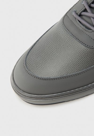 Κοντινό πλάνο μύτης παπουτσιού από γκρι δέρμα με υφή και λείο φινίρισμα, με γκρι κορδόνια που ταιριάζουν και ραμμένες λεπτομέρειες σε λευκό φόντο.