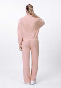 Set de pijamale roz, moi și pufoase, compus dintr-un pulover cu guler și pantaloni largi asortați. Design simplu, fără modele vizibile.