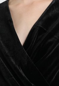 Rochie din catifea neagră, cu decolteu adânc în V și o textură moale, fină. Materialul are un ușor luciu, creând un aspect luxos.