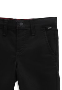 Czarne spodnie Vans z bliska, pokazujące przedni guzik, szlufki na pasek, przednie kieszenie oraz małą metkę Vans na prawej kieszeni.