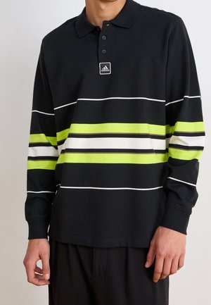 Mann trägt schwarzes Langarm-Polo mit weißen, limettengrünen und schwarzen horizontalen Streifen und Adidas-Logo auf der Brust.