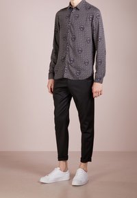 Camicia a maniche lunghe nera con motivo geometrico, abbinata a pantaloni neri e sneakers bianchi, che presenta un look casual.