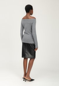 Grijze off-the-shoulder trui met lange mouwen, gecombineerd met een zwarte leren kokerrok met gestudeerde zoom en zwarte puntige hakken.