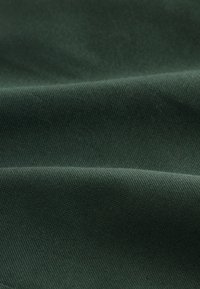 Donkergroene stof met een gestructureerde weving, close-up getoond met zachte plooien en schaduwen die de materiaaldetails benadrukken.