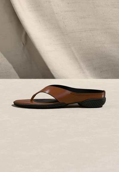 Καφέ δερμάτινο σανδάλι με λουράκι, μαύρη περιμετρική σόλα, χαμηλό τακούνι και λείο εσωτερικό φόντο.