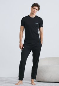 Īsas melnas piedurknes T-krekls un saskaņotas bikses. Mīksts, elastīgs materiāls ar vieglu logotipa detaļu uz krekla krūtīm. Ikdienas piegrieztne.